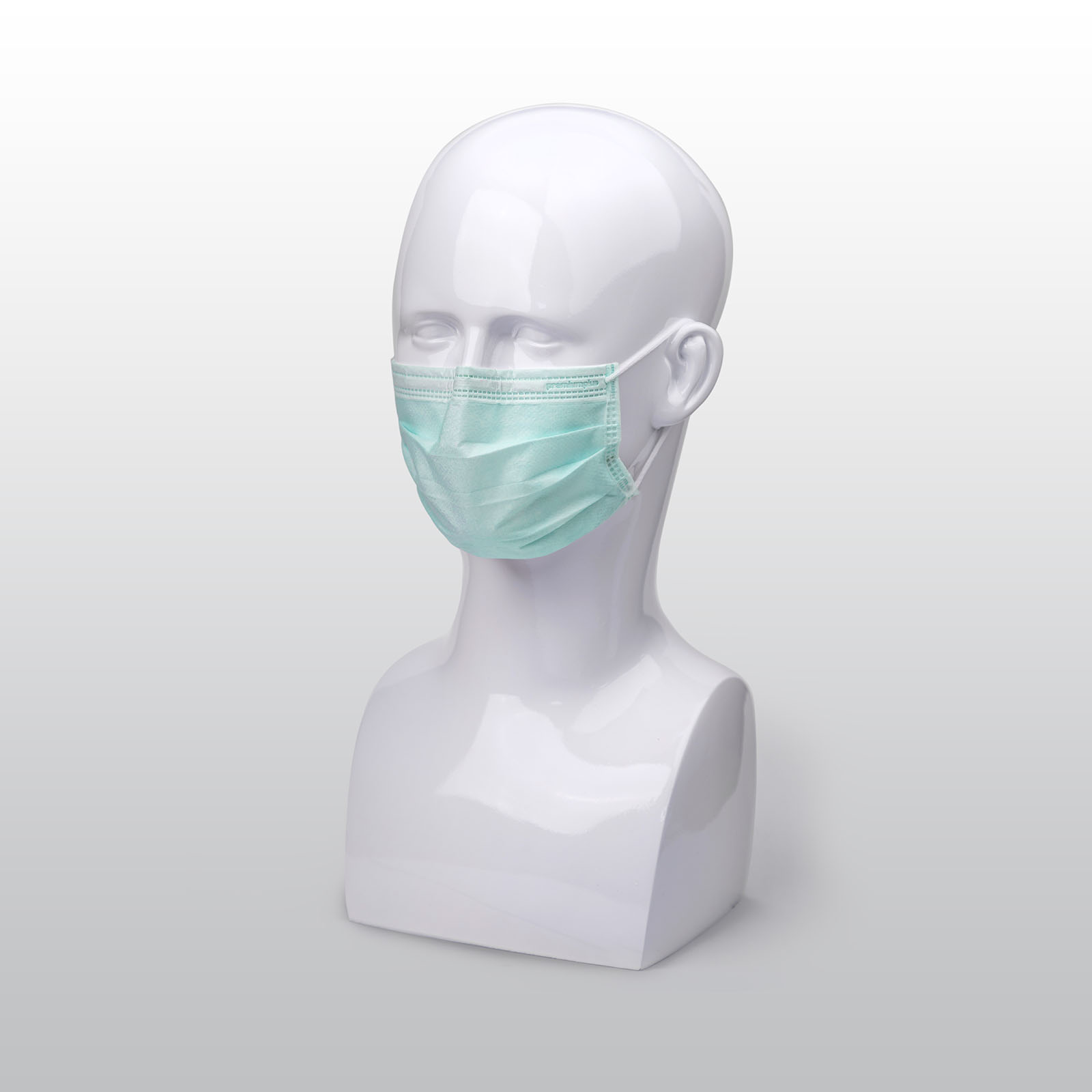Grüne Premium Plus OP-Maske auf einem weißen Modellkopf, mit elastischen Ohrschlaufen und Nasenbügel für optimalen Sitz. Für den medizinischen Einsatz geeignet.
