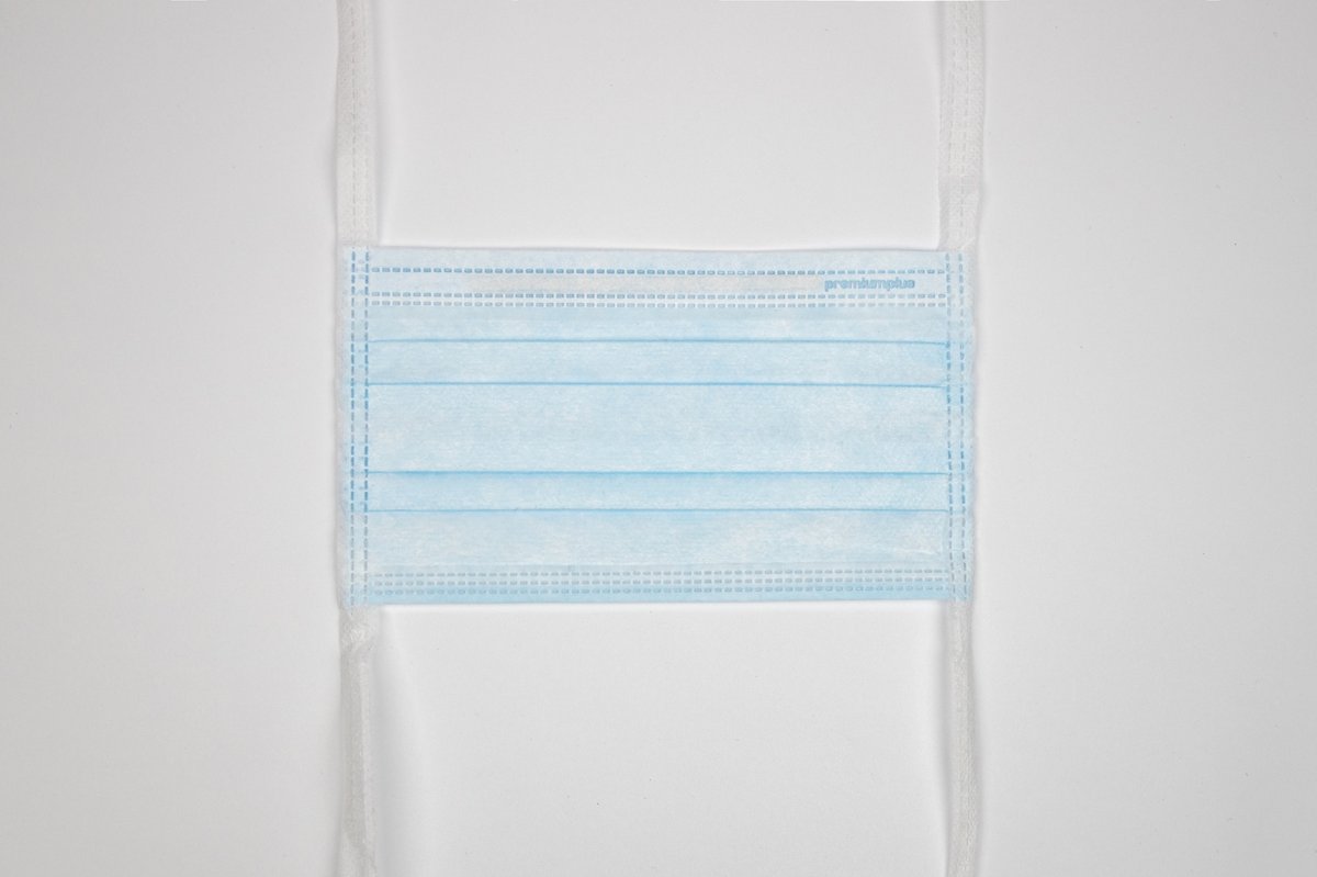 Flachliegende Premium Plus OP-Maske mit langen weißen Kopfbändern und blauem 3-lagigem Maskenkörper. Ansicht von oben auf weißem Hintergrund.